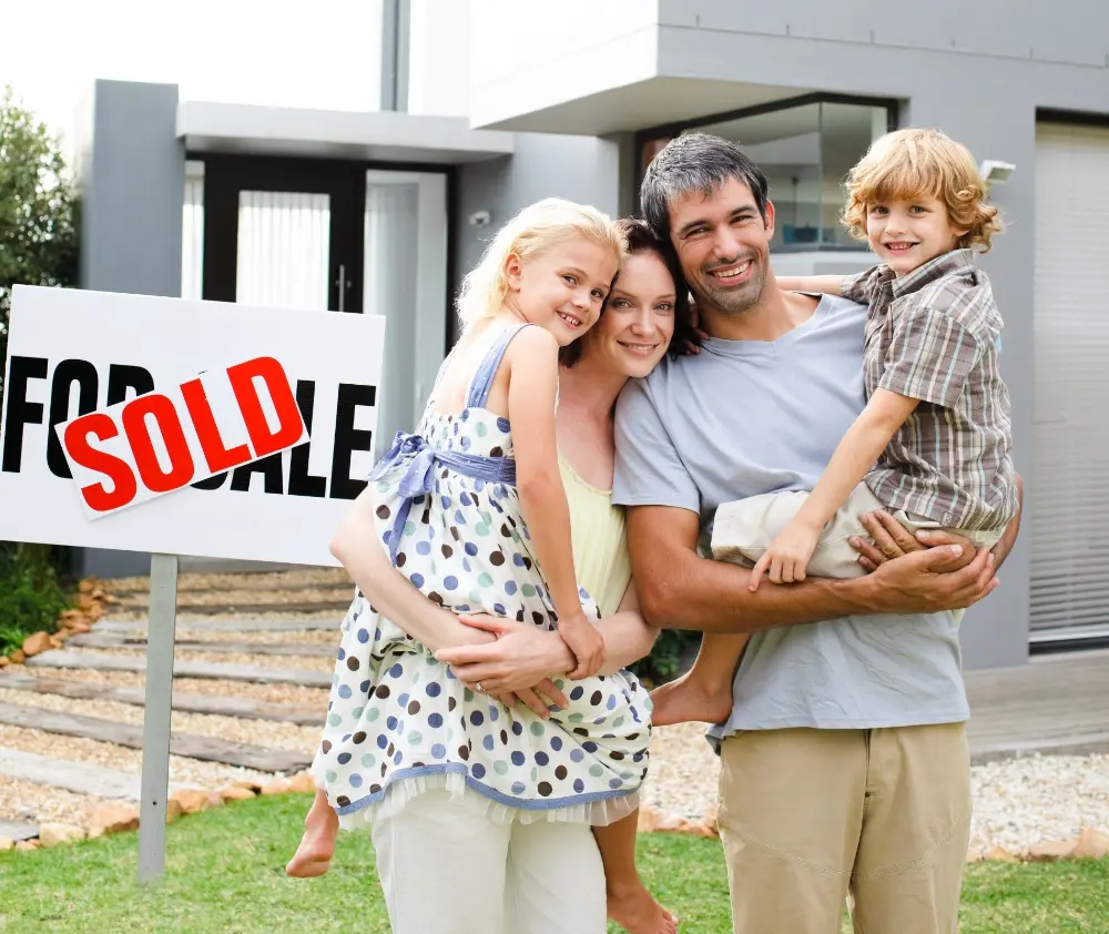 Smiling Family standing in front of a Sold sign for a house